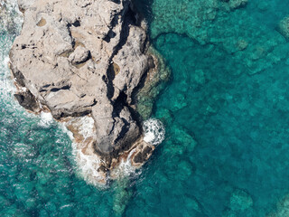 Aerial top view of sea waves hitting rocks on the beach with turquoise sea water. Sea waves on the wild rocky coast. Seascape. Travel concept. Aegean Sea, Turkey. Postcard view. Drone shot