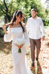 beautiful young bride in the foreground holds a white bouquet in her hands, behind the man goes to her