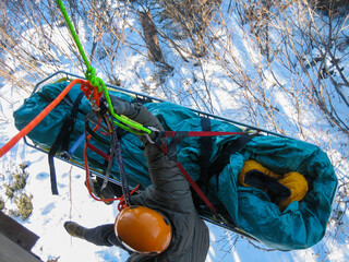 High Angle Rescue Technician Hanging From Stokes Litter Basket Above Snow Covered Terrain