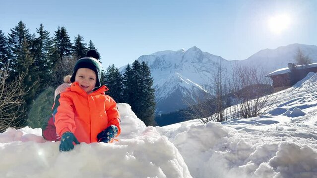 Baby girl play snowball sitting in snow fortress over mountains