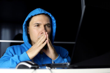 Man in and blue hoodie sitting at laptop with a thoughtful face expression. Concept of solving a...