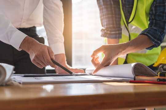 Builder team, hand of asian, caucasian young engineer, architect two man are discussing construction, use laptop computer follow project to build an industrial plan at site. Engineering worker people.