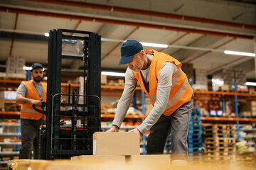 Fototapeta na wymiar Mature worker stacking cardboard boxes while working with coworker at storage compartment.
