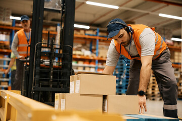 Warehouse worker organizing shipment boxes with his coworker at distribution compartment.