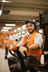 Happy worker racking up packages with pallet jack in warehouse and looking at camera.