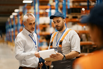 Young worker and warehouse manager analyzing reports at industrial storage compartment.