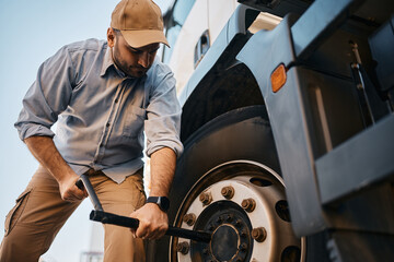 Young truck driver changing flat tire on his truck.