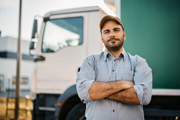 Truck driver standing with arms crossed in front of his truck and looking at camera.