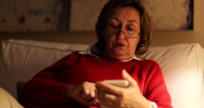 Older Person Staring At Smartphone Screen At Night Sitting On Sofa At Home