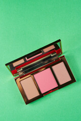 face contouring palette. bronzer, blush and highlighter in a gold palette on a green background.