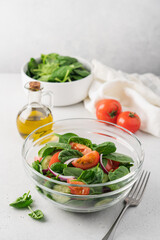 Fresh salad in  glass transparent bowl on white background. Spinach, tomato, cucumber, onion fresh vegetables for vegan, healthy diet