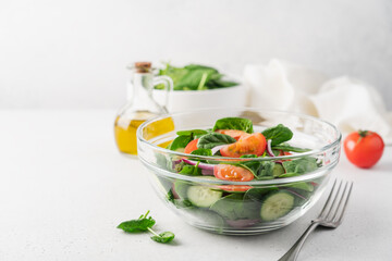 Fresh salad in  glass transparent bowl on white background. Spinach, tomato, cucumber, onion fresh vegetables for vegan, healthy diet