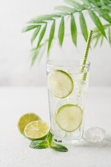 Lime mojito or lemonade with ice in tall glass  with straw on light gray background with copy space. Summer refreshing drink