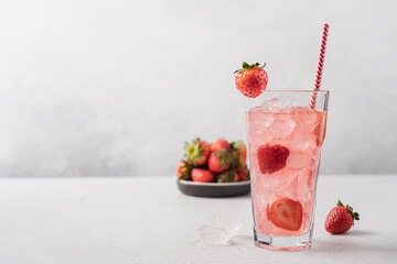 Strawberry lemonade with ice in tall glass on light gray background. Berry refreshing summer drink with straw