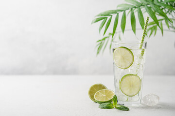 Lime mojito or lemonade with ice in tall glass  with straw on light gray background with copy space. Summer refreshing drink