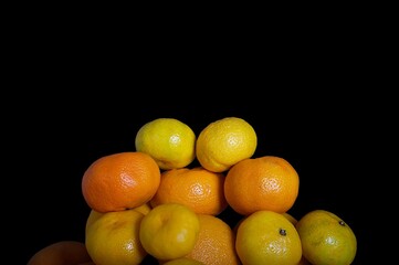 Ripe juicy oranges of a fresh harvest are stacked in a large pyramid on a plate in a photo studio with a black background.