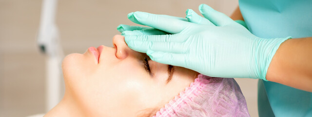 Cosmetologist with gloved hands applies a moisturizing mask with peeling cream on the female face. Facial cosmetology treatment. Procedures for facial care