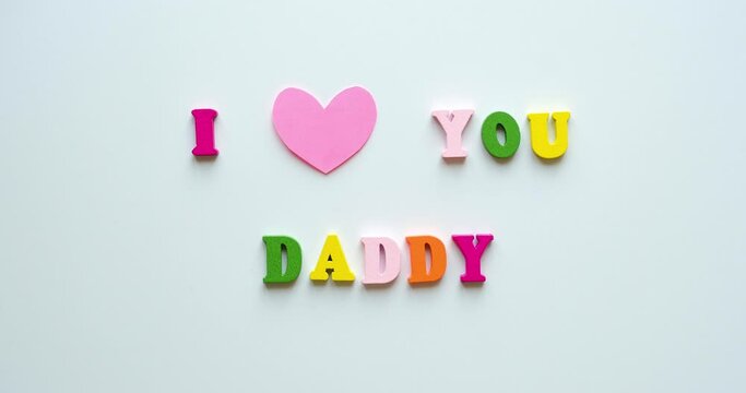 Phrase I Love You Daddy from colorful wooden letters and a beating pink heart. Congratulations on father's day. 4K looped stop motion animation