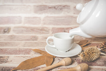 Tea concept, white teapot with white tea cup with dry leaves on wooden background.