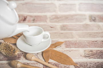 Tea concept, white teapot with white tea cup with dry leaves on wooden background.