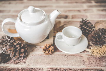 Tea concept, white teapot with white tea cup with dry leaves on wooden background.