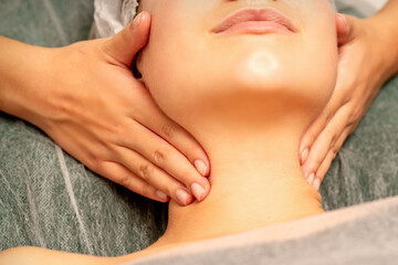 Naklejka premium Facial massage. Hands of a masseur massaging neck of a young caucasian woman in a spa salon, the concept of health massage