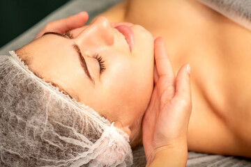 Fototapeta na wymiar Facial massage. Hands of a masseur massaging neck of a young caucasian woman in a spa salon, the concept of health massage