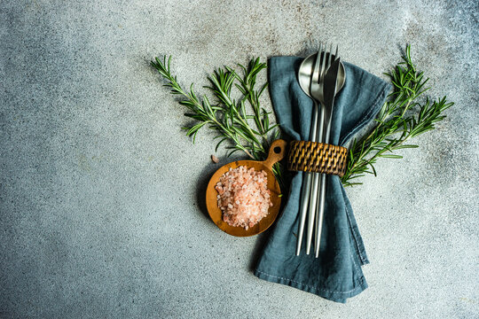 Overhead view of a rustic cutlery setting with pink himalayan salt and a sprig of rosemary