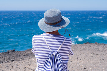 Rear view of mature woman dressed in blue admiring the sea looking at horizon over water. Mature...