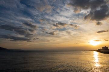 Sunset reflects in calm ocean water as clouds pass overhead