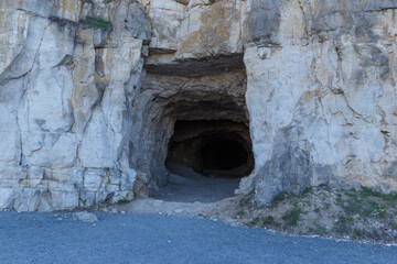 Obraz premium The concept of cave people's habitat. A stone wall with a dark hole, the entrance to the cave. Historical mineral mine.