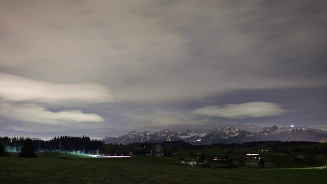 Ammergau Alps and farm near road at cloudy night time lapse