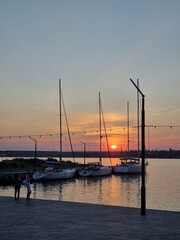 Fototapeta na wymiar Mykolaiv, Ukraine - . September 4, 2021. Gorgeous Golden hour sunset with boats and yachts at dusk on the river shore. the sun rays of the evening light and sunlight. People walking at the Yachts-club