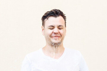 Wet young caucasian man in white t shirt with closed eyes and water is flowing from his face....