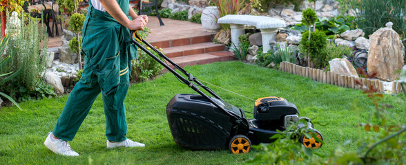 Young gardener mowing the lawn with lawnmower in summer