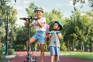Portrait of two cute blond little caucasian sibling kids girl wear safety helmet enjoy having fun riding electric scooter city street park outdoors sunny day. Healthy sport children activity outside © Kyryl Gorlov