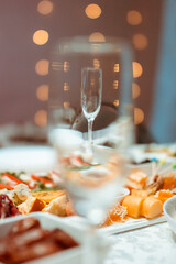 A glass is on the table and is visible through another glass against the background of garlands  