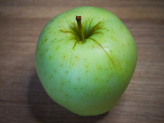 The Reinette Simirenko is an antique apple variety. The fruit has tender, crisp, greenish white flesh with a subacid flavor. A green apple on a wooden tabletop, close-up.
