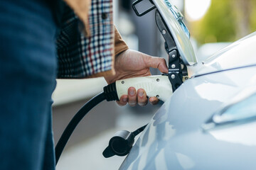 Man holding power supply cable at electric vehicle charging station. Close-up	
