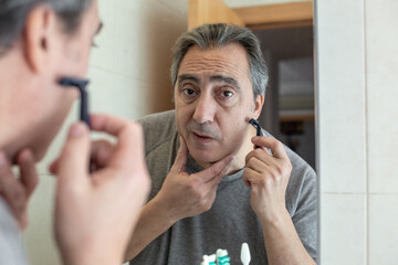 senior man shaving in front of the mirror looking at camera