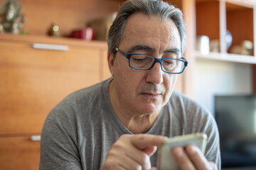 senior man at home typing messages on the phone