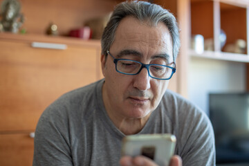 senior man at home reading messages on the phone