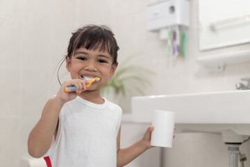 Little cute baby girl cleaning her teeth with a toothbrush in the bathroom