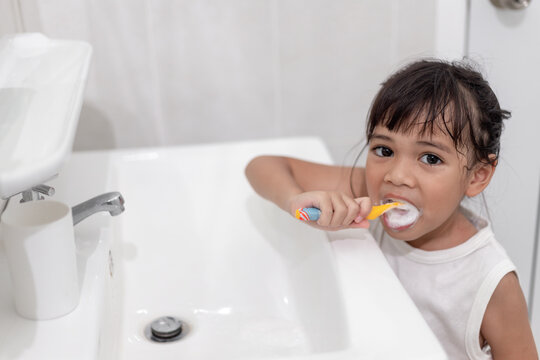 Little cute baby girl cleaning her teeth with a toothbrush in the bathroom