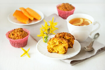 Homemade baked pastries. Healthy pumpkin muffins with traditional fall spices, pieces of pumpkin on saucer. White cup with tea on  gray linen napkin. Selective focus