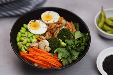 Top view of bowl with japanese udon noodles, spicy scallops, eggs, carrot, beans and sesame seeds on black bowl and gray concrete background. Flat lay, overhead 