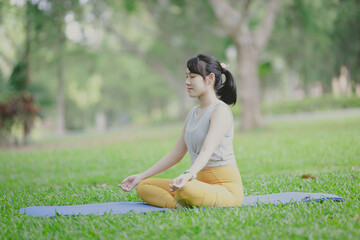 Close up of woman practice yoga meditation exercise in park, beautiful female sitting on mat for relaxed yoga posture in the morning , exercise at park, mental health care,healthy and sport