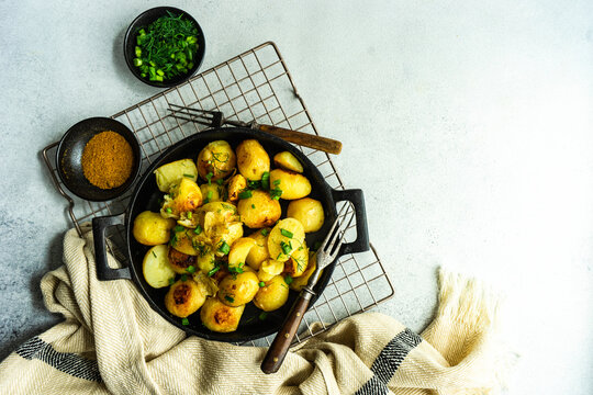 Overhead view of roasted potatoes with spring onions and dill on a cooling rack