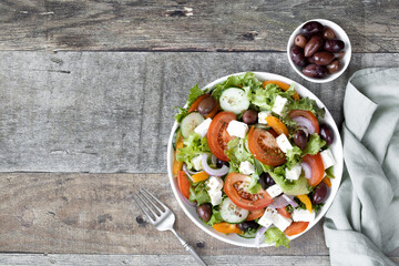Greek salad of fresh cucumbers, tomatoes, peppers, lettuce, feta cheese and olives seasoned with olive oil and spices. Top view, copy space