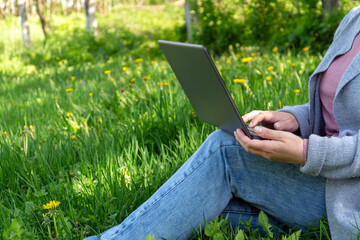Rest with a laptop in nature in the park on a sunny day against the backdrop of green grass. Woman freelancing outdoors